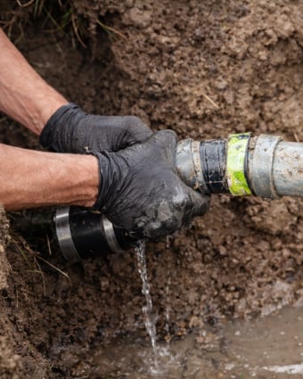 Plumber repairing pipes under a residential kitchen sink with tools and gloves.