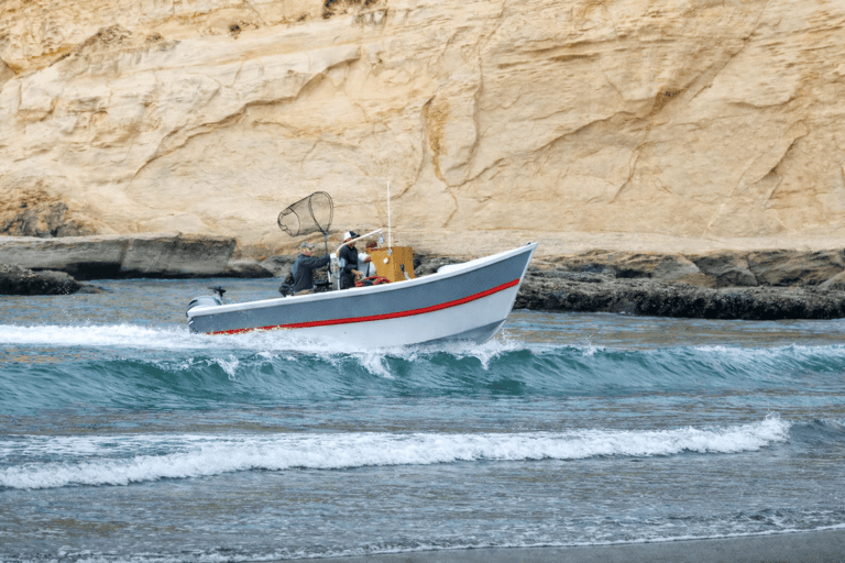 Small dory fishing boat cruising near rocky coastline.