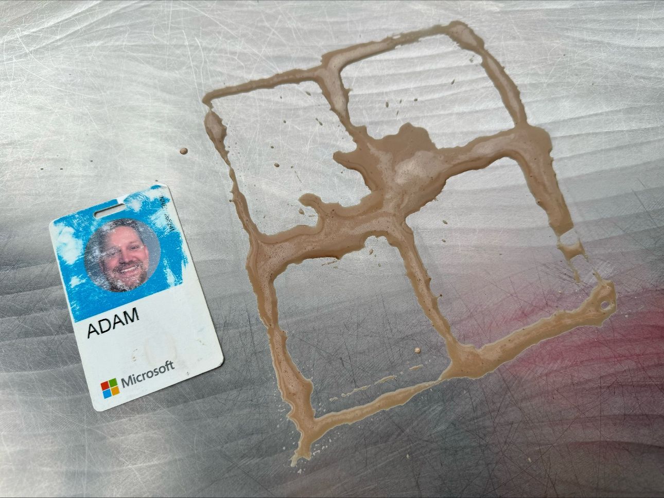 Adam's badge on the table next to a Windows logo drawn in coffee