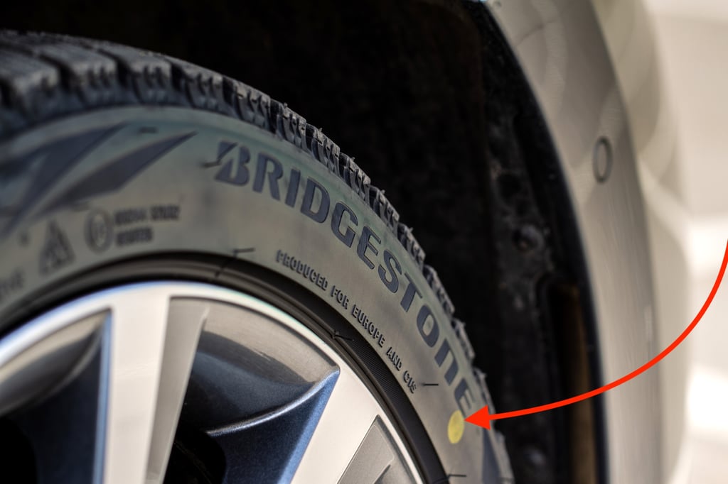 Close-up of a Bridgestone tire with a yellow dot marking and a red arrow pointing to it.