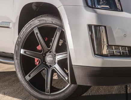 Close-up of a KMC brand alloy wheel with a silver and black finish, featuring a red brake caliper, on a silver SUV with a visible headlight and grille elements.