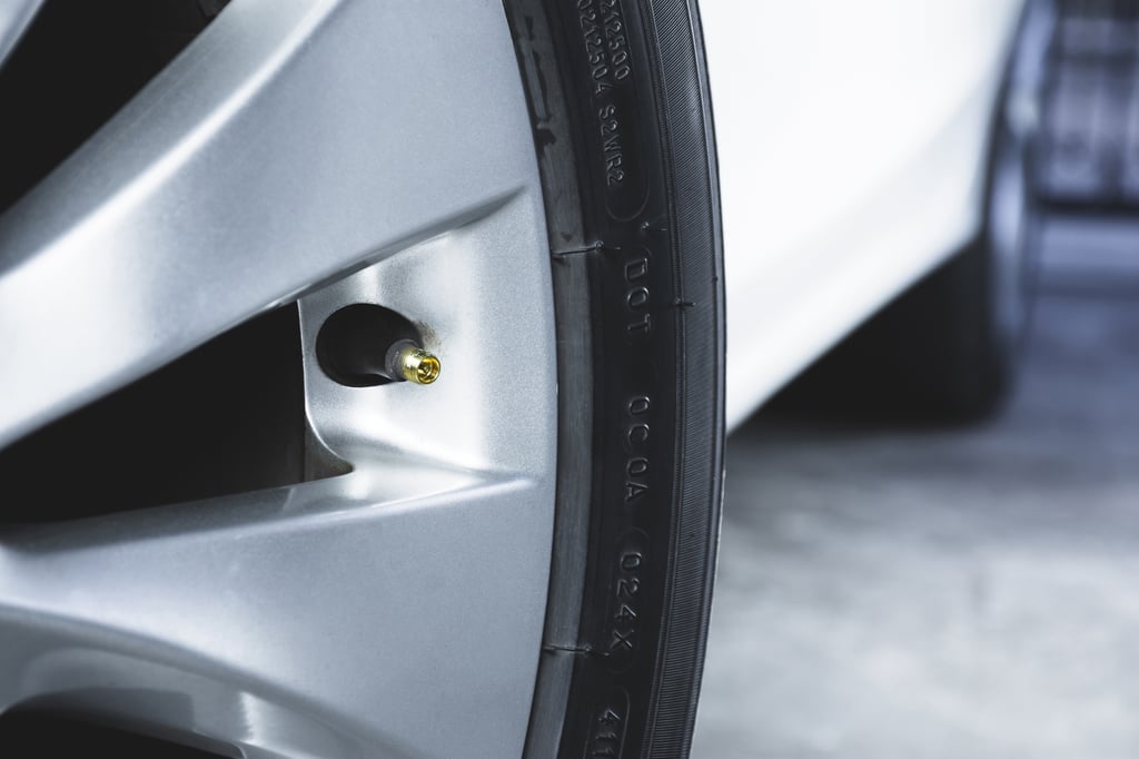 Close-up view of a car tire's rim with a visible air valve stem and a missing cap.