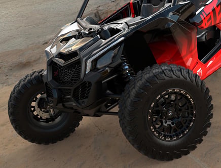 A close-up of a rugged off-road vehicle featuring large, textured tires, a black front grille with a red emblem, and a partial view of its red and black body. The vehicle is parked on a rough terrain surface.