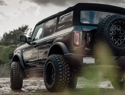 Black Ford Bronco with large off-road tires, photographed from the rear, outdoors.