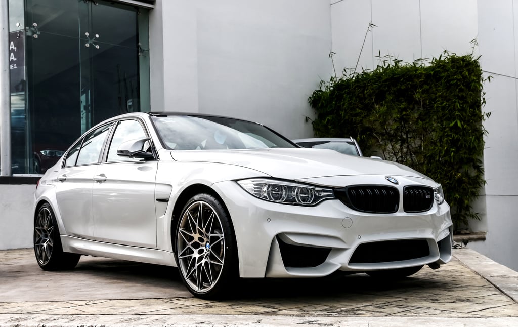A white BMW sedan parked in front of a modern building with glass windows and a green plant growing on the wall.
