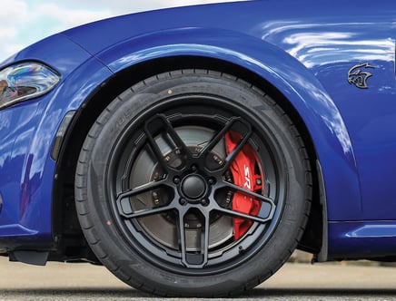 A close-up view of the front wheel of a blue car with a black rim and a red brake caliper labeled "SRT."