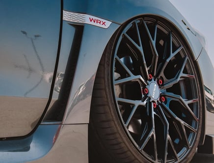 Close-up of a car with a blue finish featuring a stylish alloy wheel with red accents and a WRX badge above the fender.