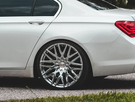 Close-up of a white car's rear wheel with shiny chrome alloy rims parked on a road.