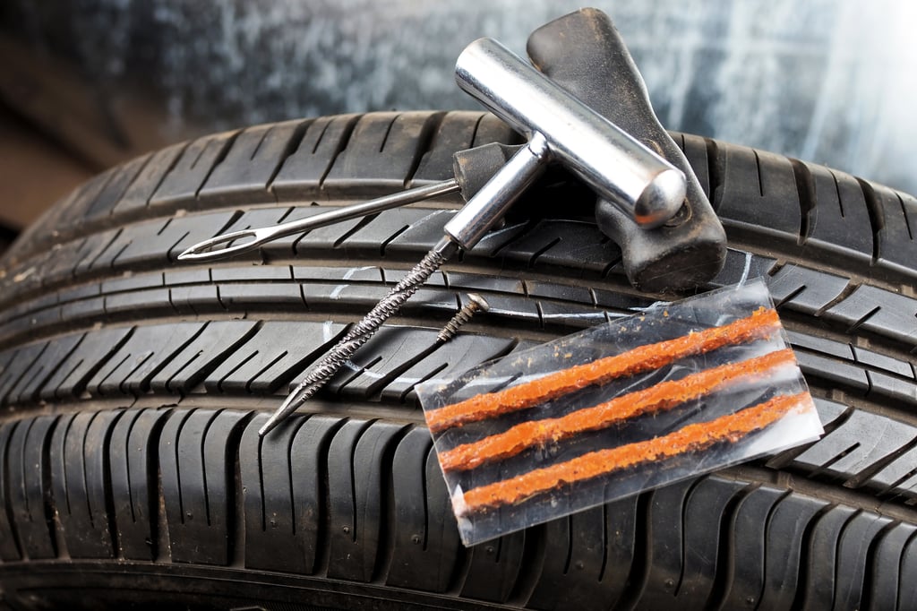 A car tire with a puncture repair kit on top, including a T-handle insertion tool, a spiral probe tool, a screw, and repair strings in a plastic sleeve.