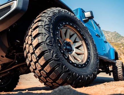 Close-up of a rugged off-road tire on a blue vehicle, set against a mountainous backdrop.