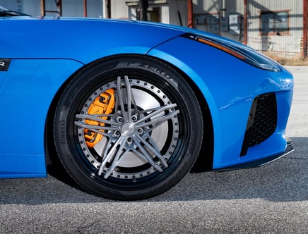 Close-up of a blue car's front wheel, featuring Pirelli tires, large silver alloy rims, and orange brake calipers.