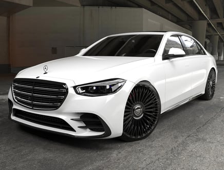 A white luxury sedan with a distinctive front grille and sleek design, parked indoors on a concrete surface.
