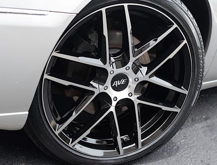 Close-up of a black and silver alloy wheel on a car, featuring a multi-spoke design and embossed 'AVE' logo at the center.