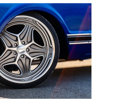 Close-up of a polished chrome car wheel with a distinctive, curving spoke design on a blue vehicle, captured against a pavement background.