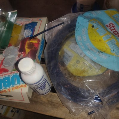 Coiled blue garden hose with cleaning supplies and hardware - Image 1 of 2