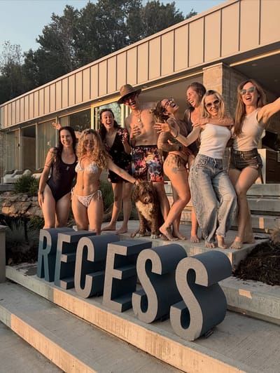 Amis qui rient sur les marches derrière une grande enseigne RECESS
