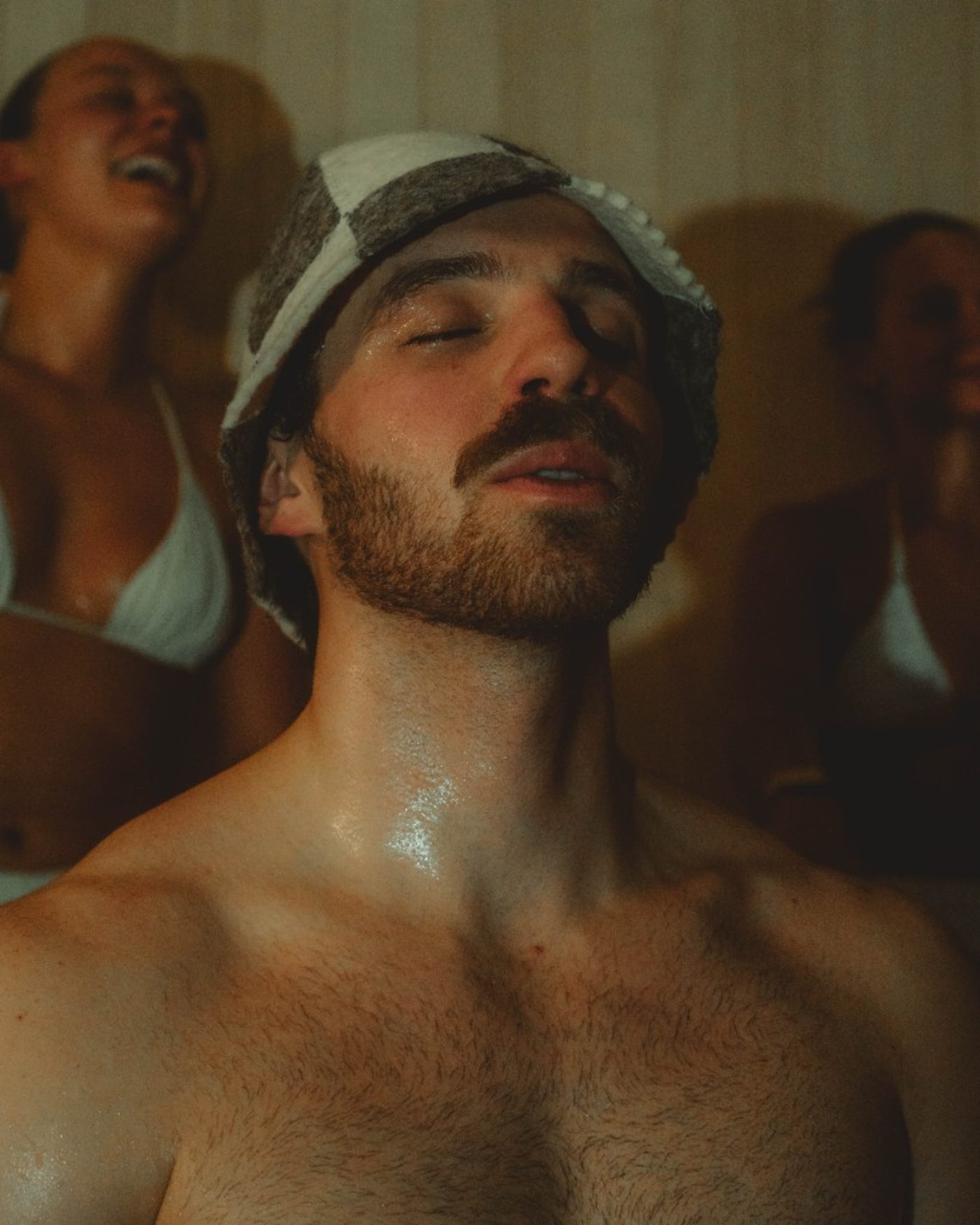 Invité dans un moment de présence calme dans le sauna RECESS, chapeau de sauna et lumière chaude.