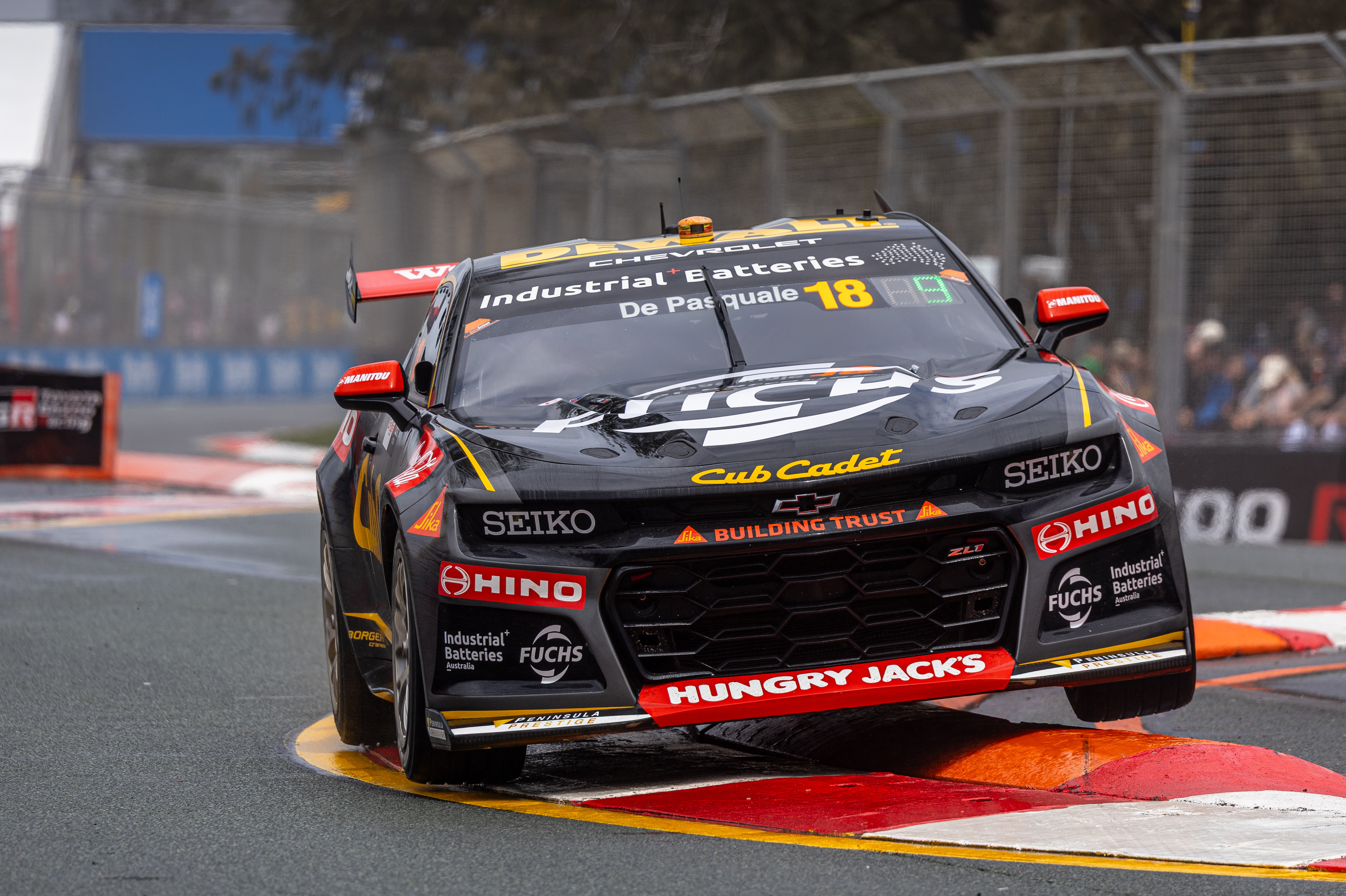 Black and gold Supercar number 18 bounces over a curb at a street circuit.