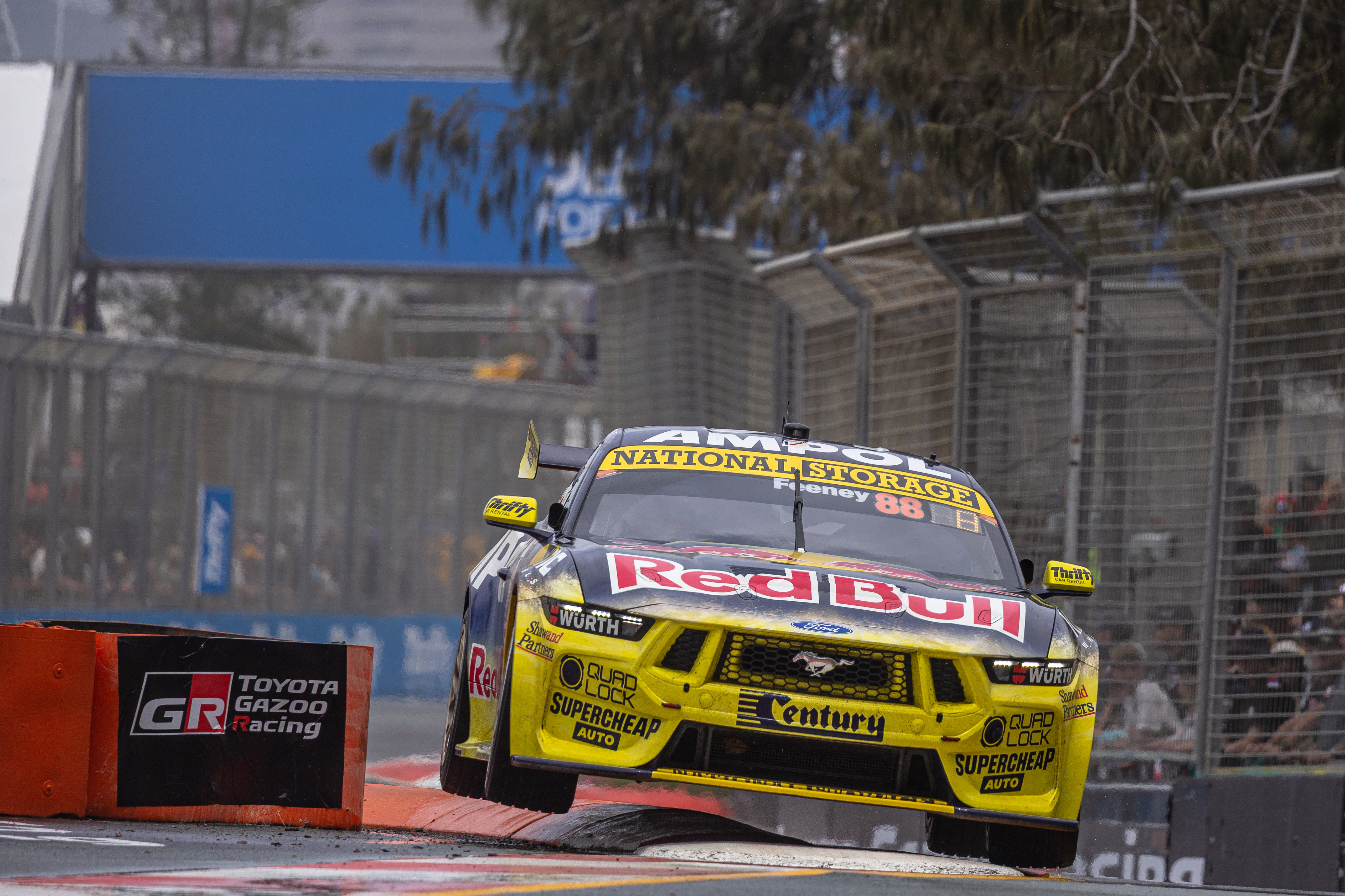 Red Bull-liveried Ford Mustang Supercar number 88 bouncing over a street circuit kerb.
