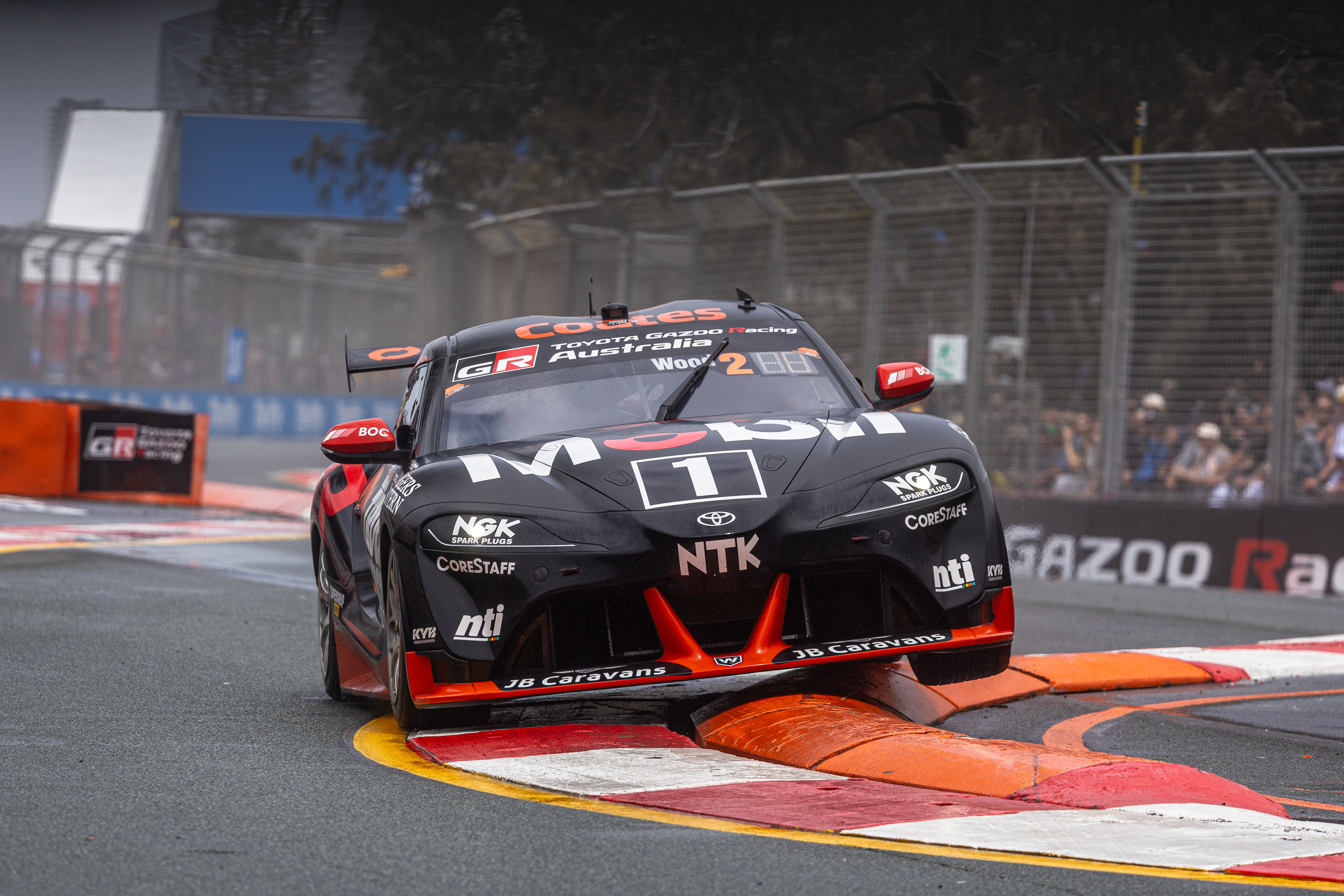 Toyota GR Supra race car number 1 bounces over a kerb on a street circuit.