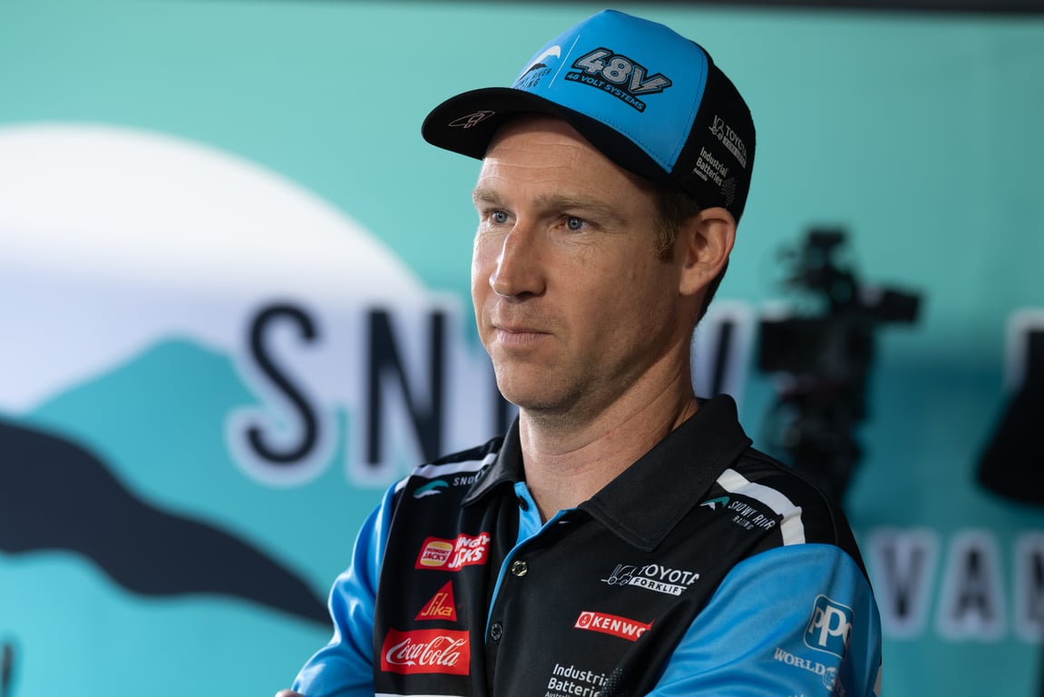David Reynolds in branded cap and shirt looking to the side in the pit lane.