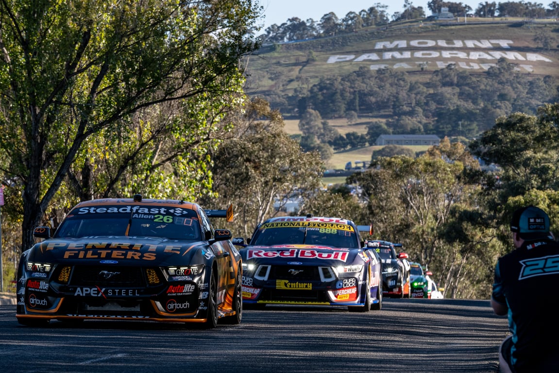 Supercars racing up Mount Panorama with the Bathurst hillside sign in the background.