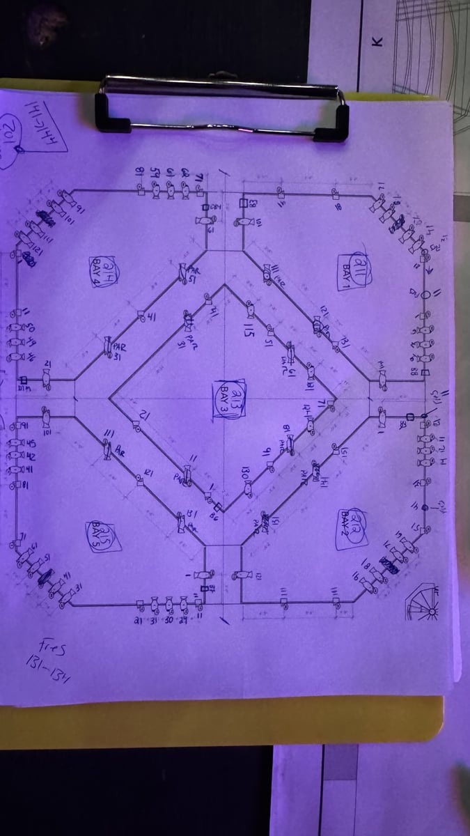 A clipboard holding a hand-marked Black Box grid hang worksheet, lit in purple stage light