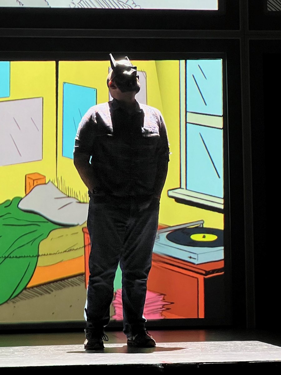 An actor in a Batman cowl in front of the show's comic-book bedroom projection.