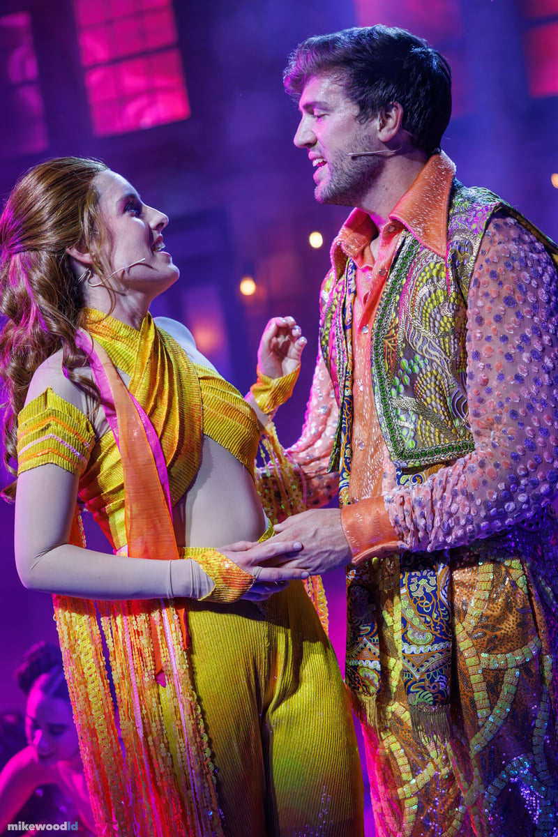Two performers share a tender moment in vibrant disco costumes during Dancin' In The Street.