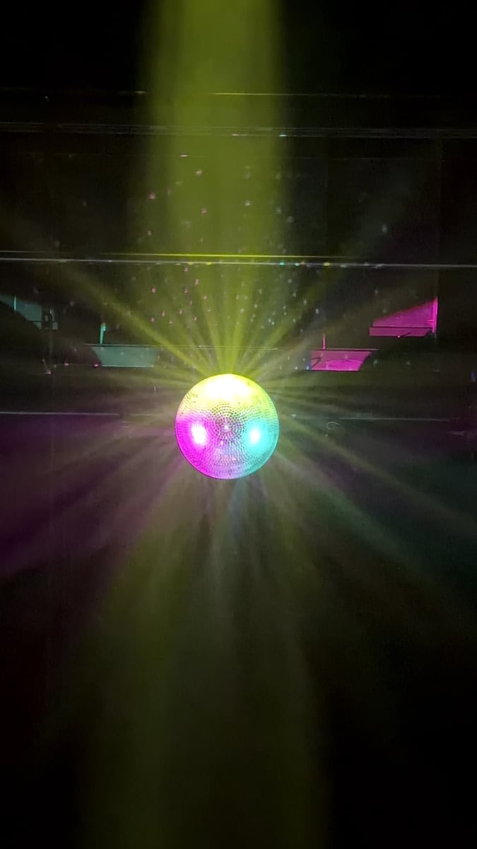 A mirror ball scatters magenta and green beams across the darkened house during a lighting test.