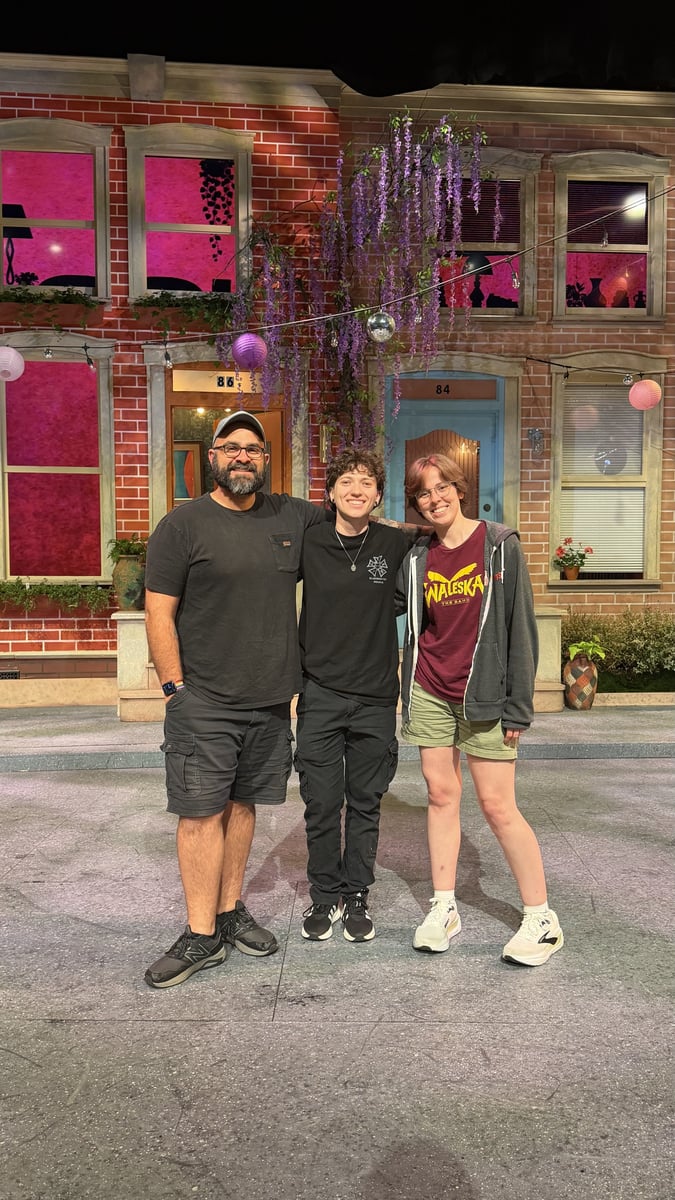 The lighting team, Mike Wood, Jay, and Mack Scales, pose in front of the brick-street set lit with pink window washes and string lights.
