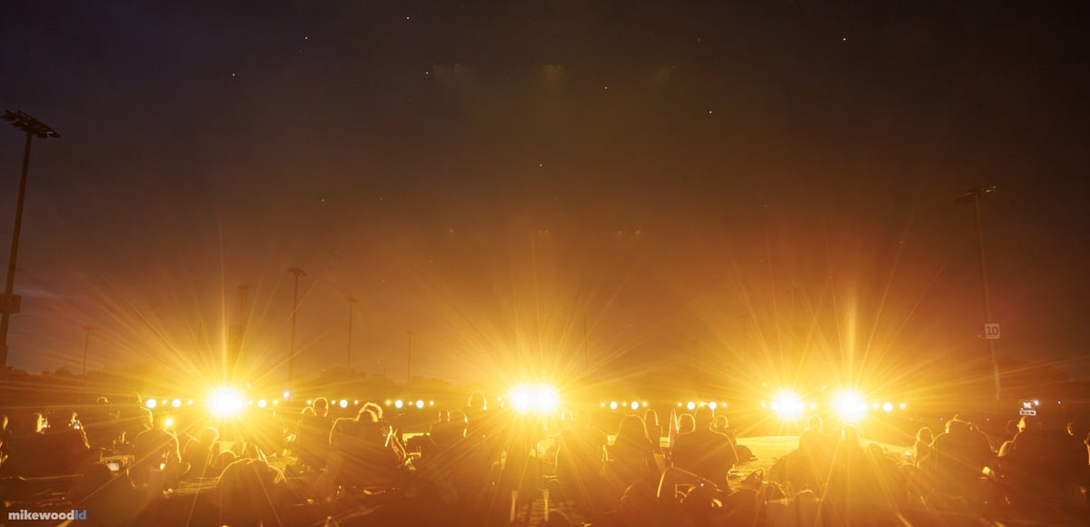 Rows of amber fixtures flaring through the seated audience on the open field, filling the night haze with gold.