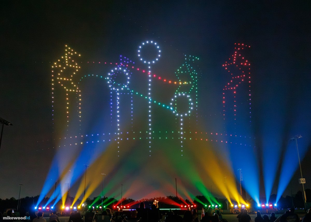 Three Quidditch goal hoops and broomstick players traced in colored drones, blue, gold, green, and red beams below.
