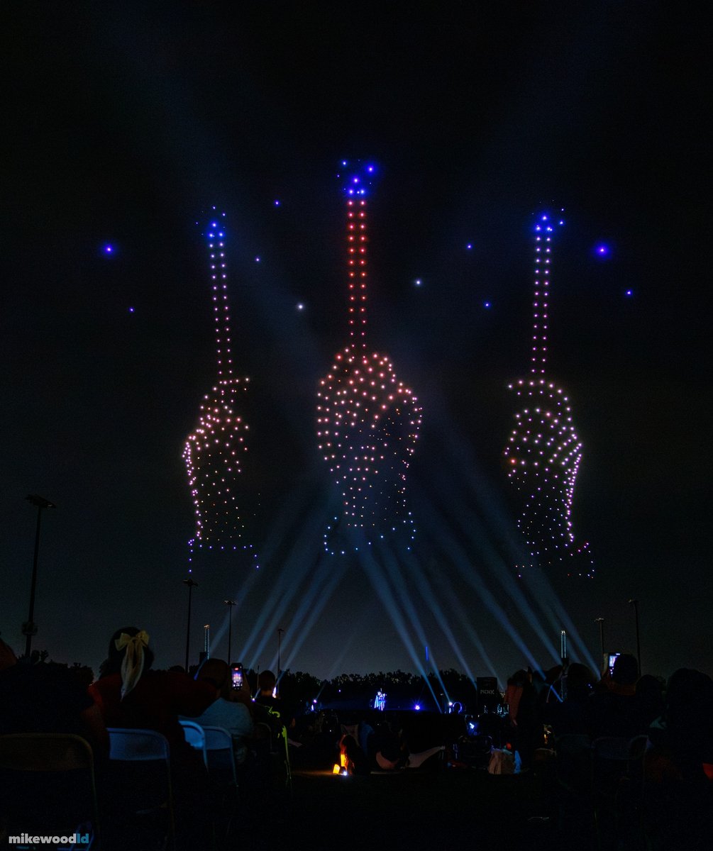 Three raised wands with glowing tips rendered in drones, white beams crossing beneath them.