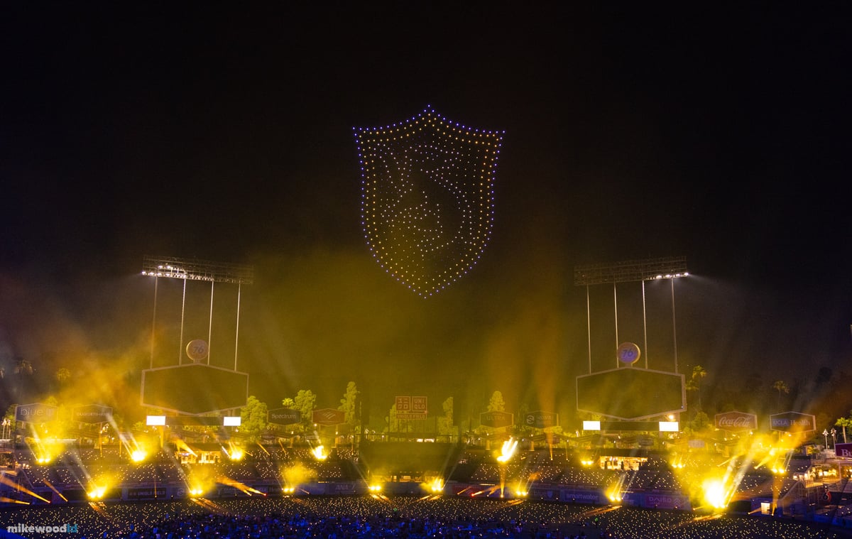 A house crest in blue drones above the stage as towering amber beams erupt from the ground through the haze.