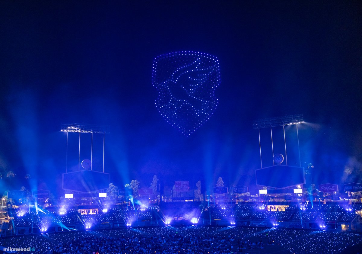 A house crest rendered in blue drones above Dodger Stadium, the entire bowl and crowd washed in matching deep blue.