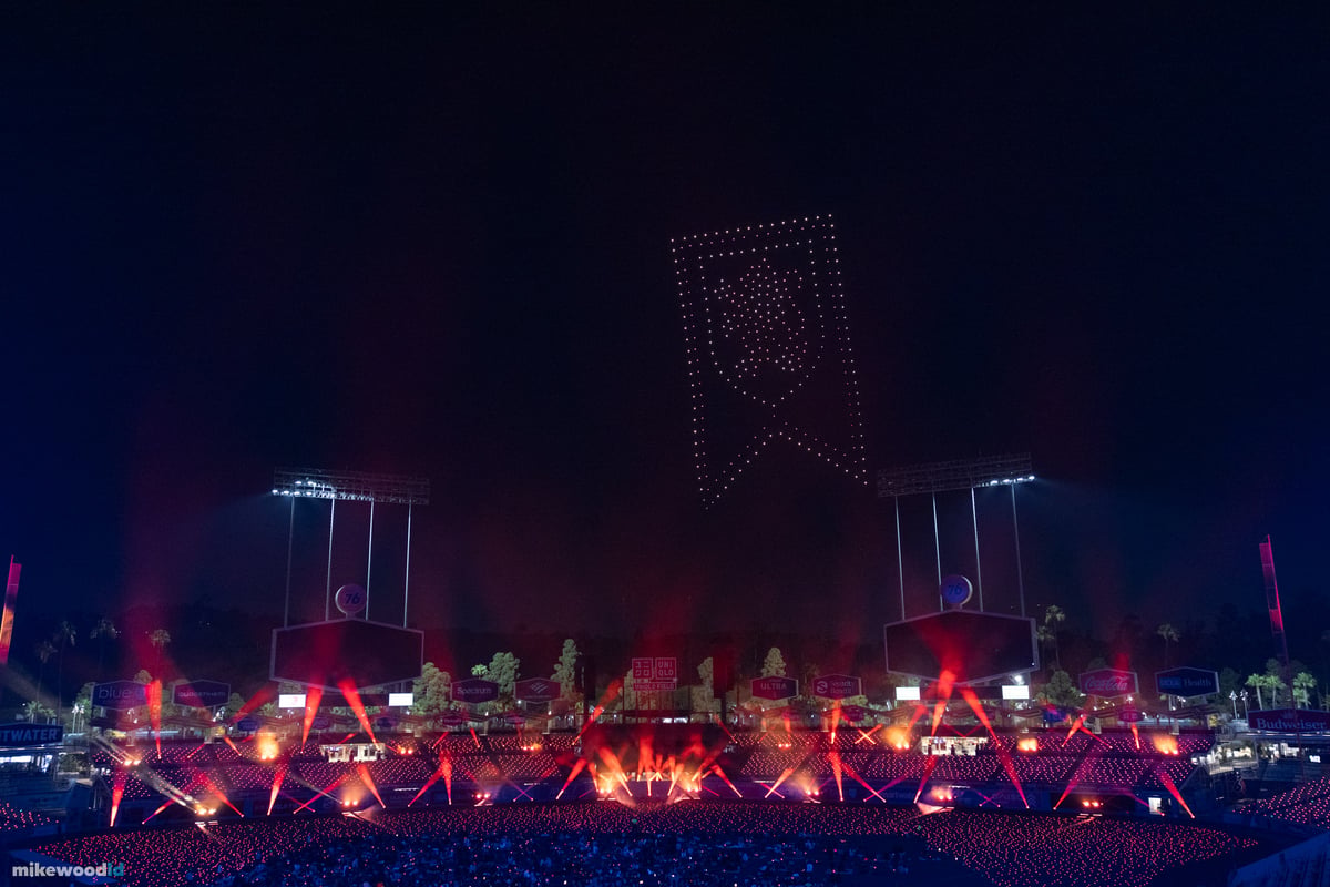A red house banner rendered in drones above the stadium, red beams fanning up from the stage and crowd.