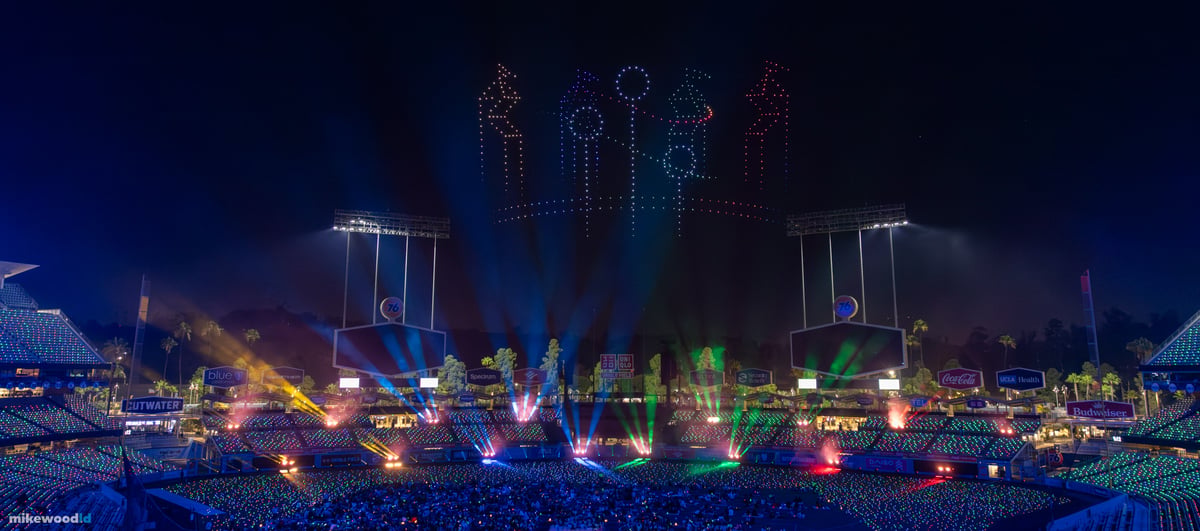 A row of Harry Potter character figures rendered in drones above Dodger Stadium, multicolored beams sweeping across the crowd.
