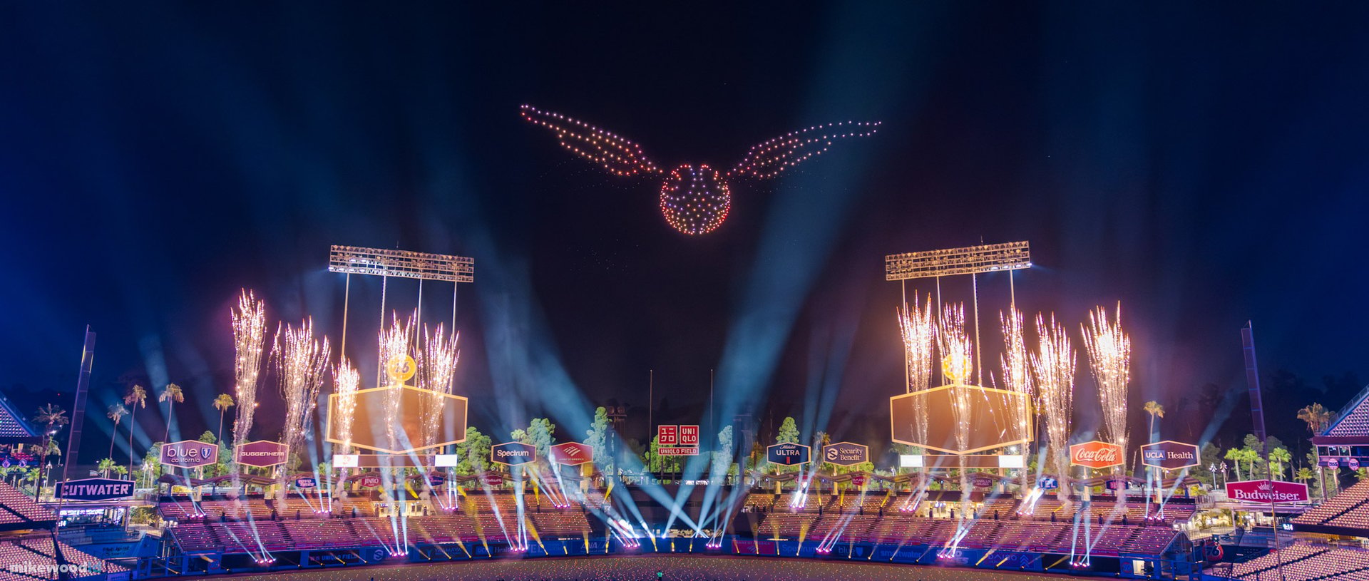 The Golden Snitch, a winged orb in amber drones, hovering above the stage as gold pyrotechnic fountains erupt across the stadium.