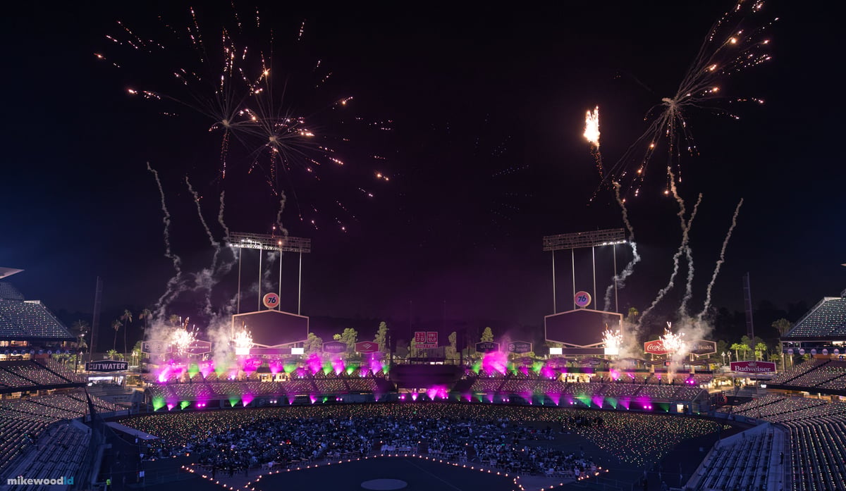 Gold fireworks bursting over the stadium as pink and green light washes the lower bowl, smoke drifting through the beams.