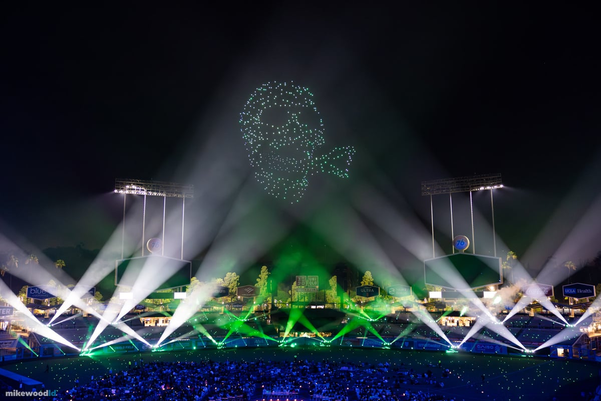 A green skull formation in drones above Dodger Stadium, crossed white beams fanning up from the stage in a symmetrical lattice.