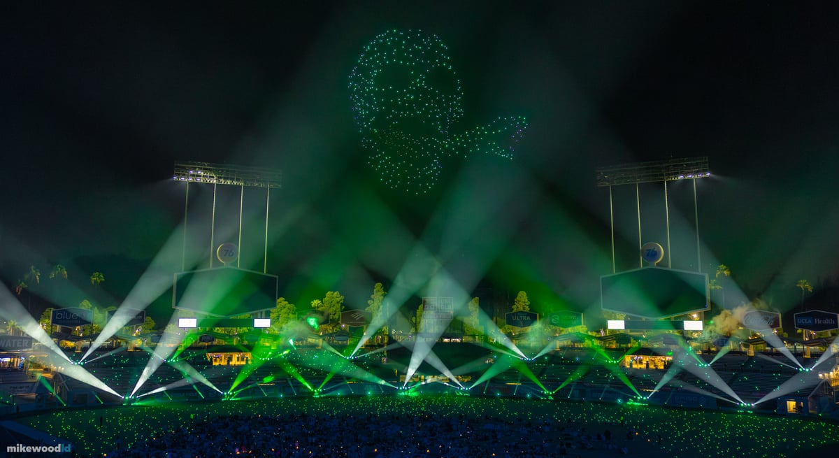 A green skull formation in drones above Dodger Stadium, green and white beams fanning up through the haze.