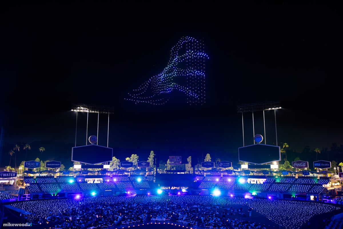 A winged creature rendered in pale blue drones high over a deep-blue Dodger Stadium at night.