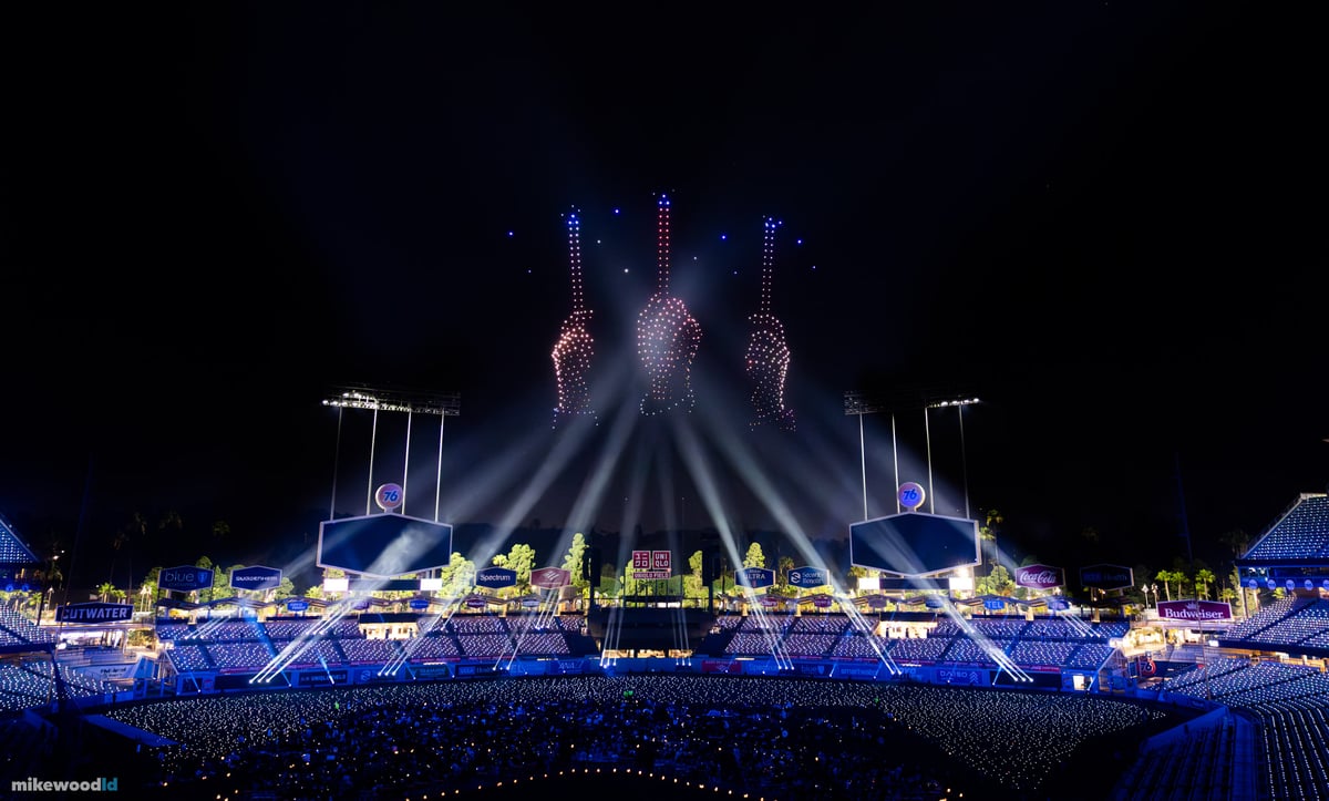 Three tall vertical formations rising in red and blue drones above the stage, white beams fanning up beneath them.