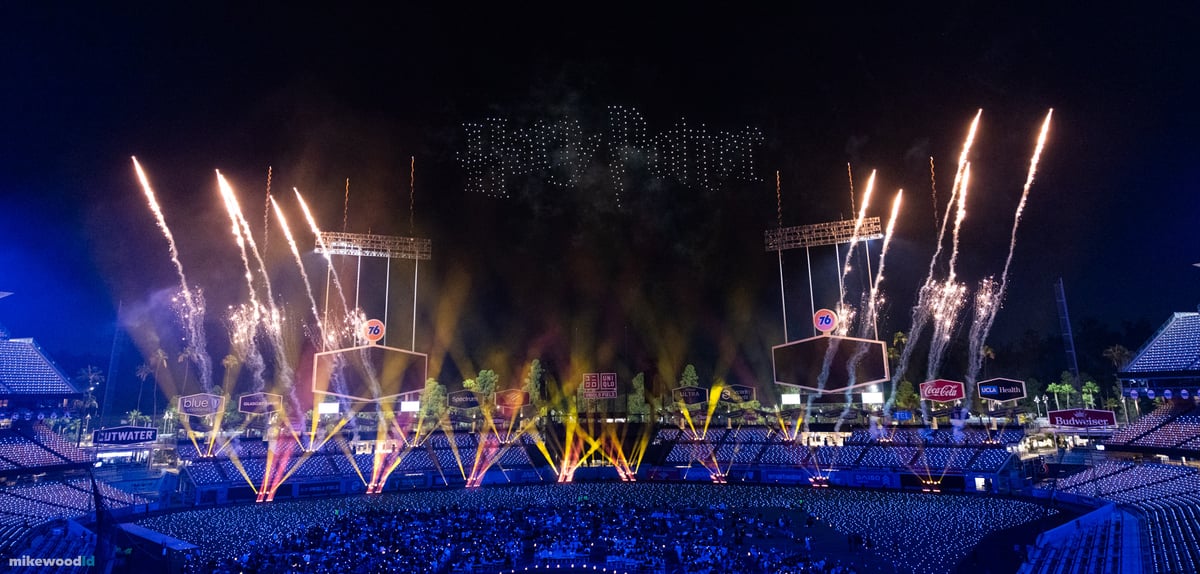 The Harry Potter title rendered in white drones above the stadium as gold pyrotechnic comets streak upward across the stage.
