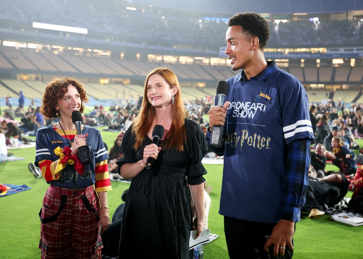 Harry Potter film actor Bonnie Wright on the field at Dodger Stadium before the show, between two DroneArt Show hosts holding microphones.