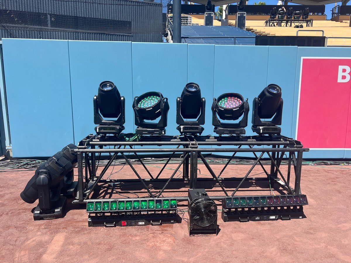 A crew member prepping a pre-rigged bar of moving lights on the field.