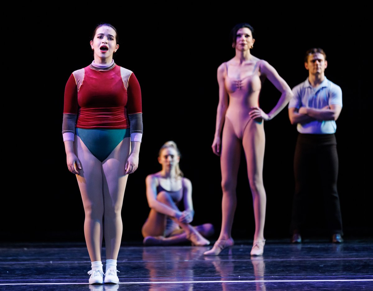 An auditioner sings downstage while three dancers watch from behind on the bare stage
