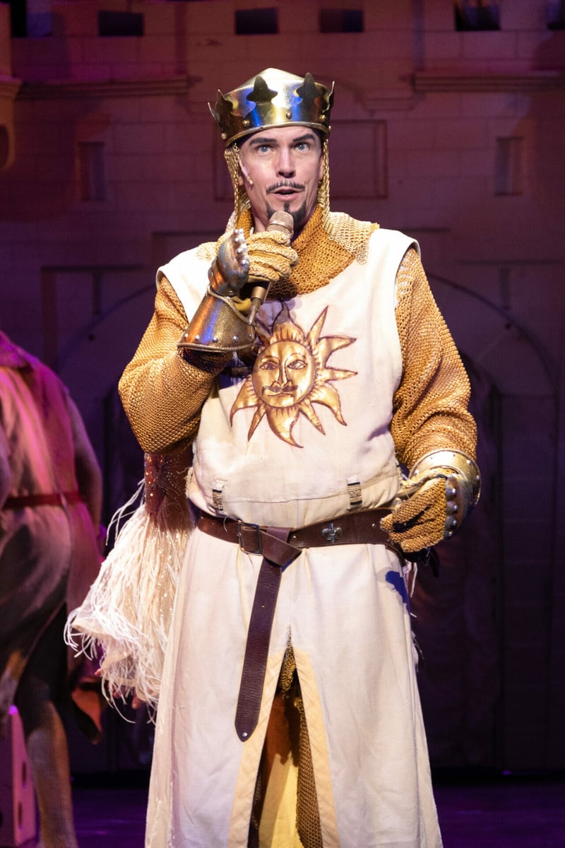Googie Uterhardt as King Arthur in crown and chain mail, singing center stage