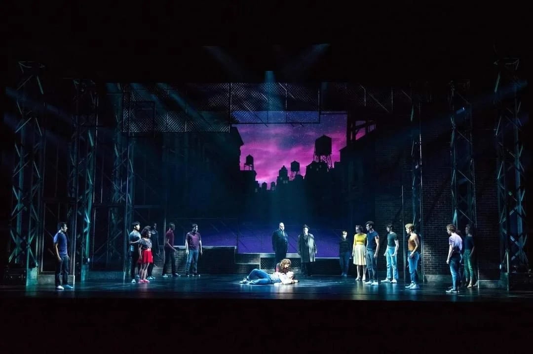 The company stands in silhouette against a purple city skyline in the final tableau
